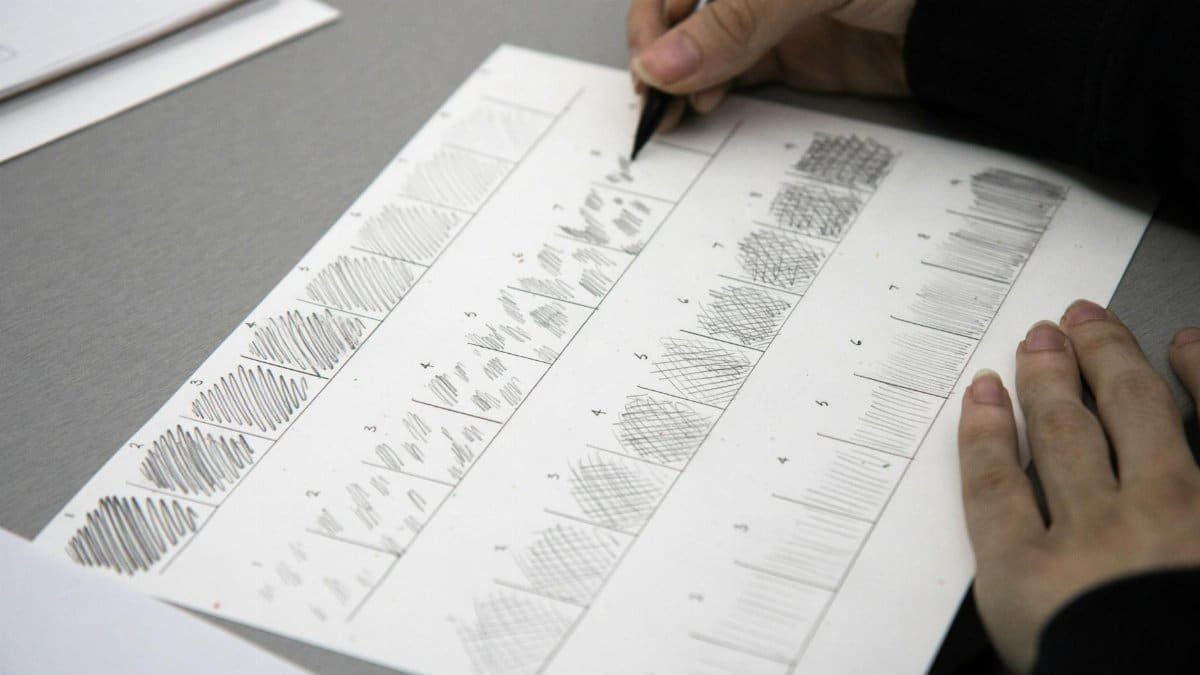 Close-up photo of hands using a pen to practice shading techniques on paper.