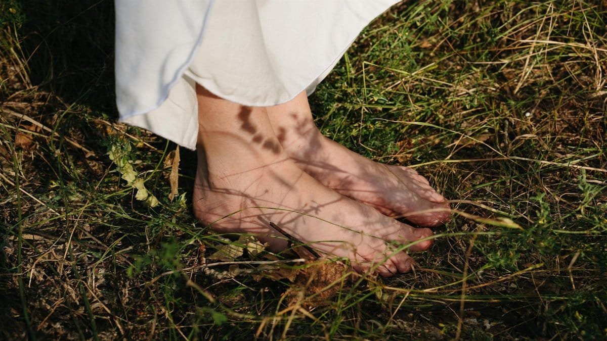 Close-up of bare feet on grass with gentle sunlight and soft shadows.