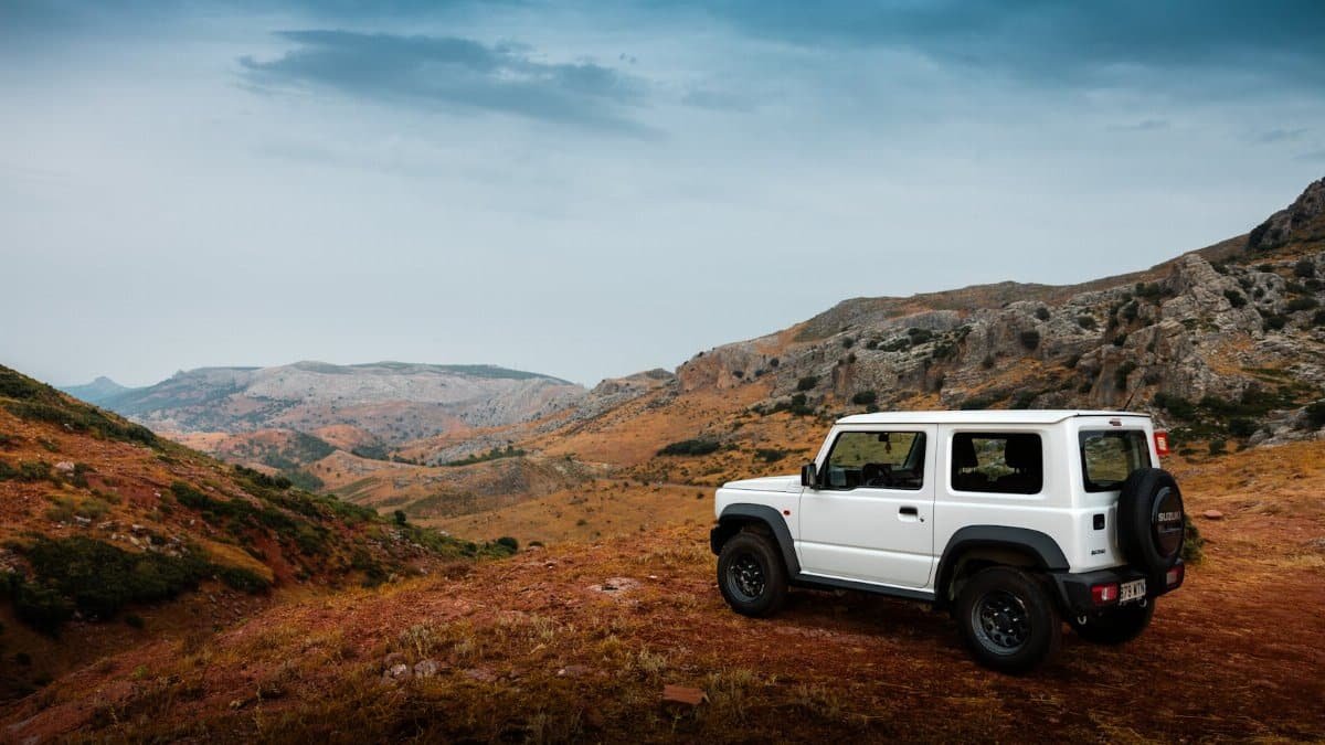 White SUV parked on a scenic mountain overlook with rocky terrain and cloudy sky.