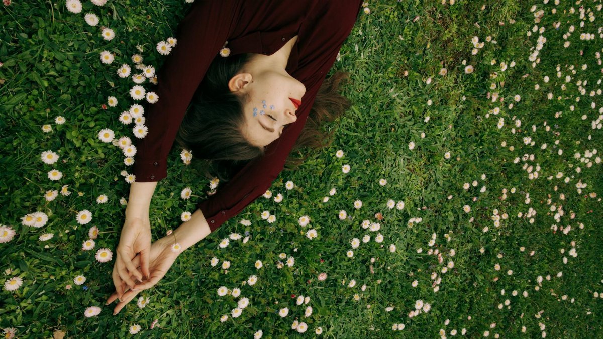 Woman lying peacefully on a grassy field with daisies, embodying relaxation and nature connection.