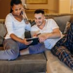 Interracial couple laughing and shopping online at home using tablet and smartphone.