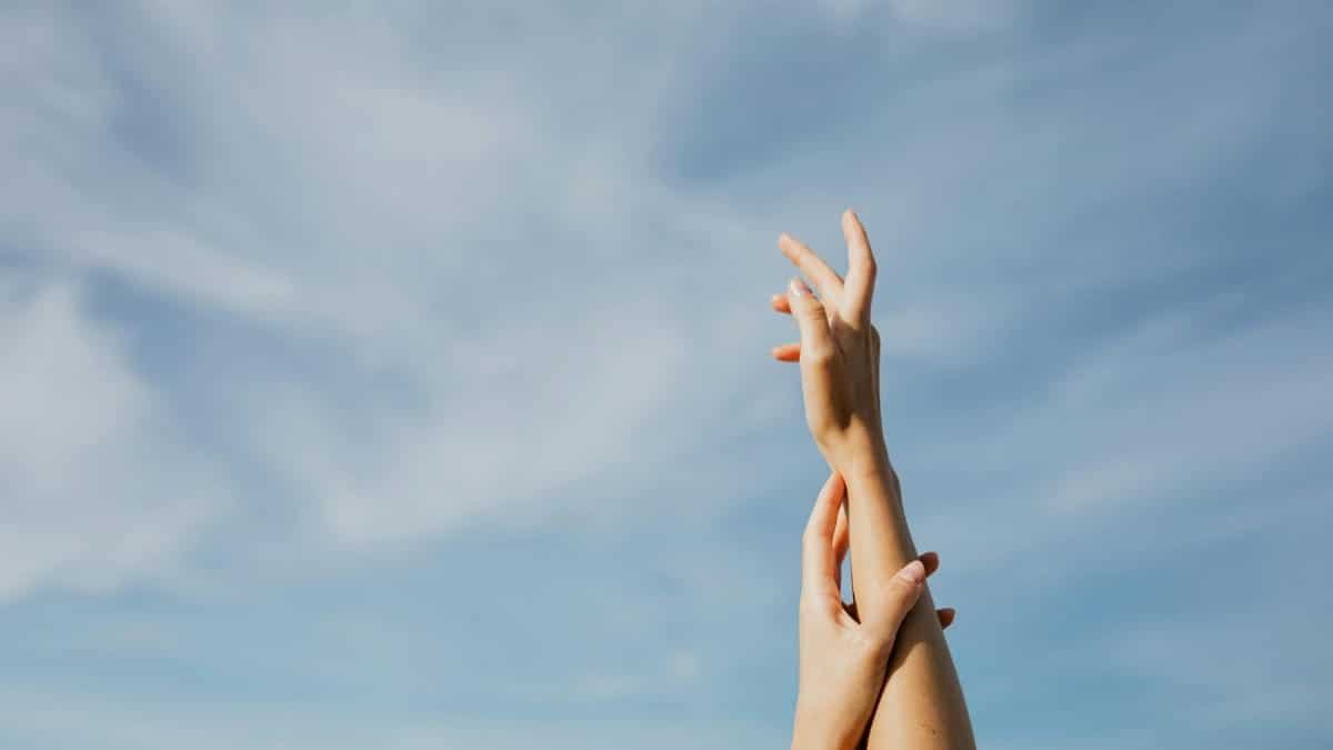 Two adult hands reaching up in front of a clear blue sky, symbolizing freedom and aspiration.