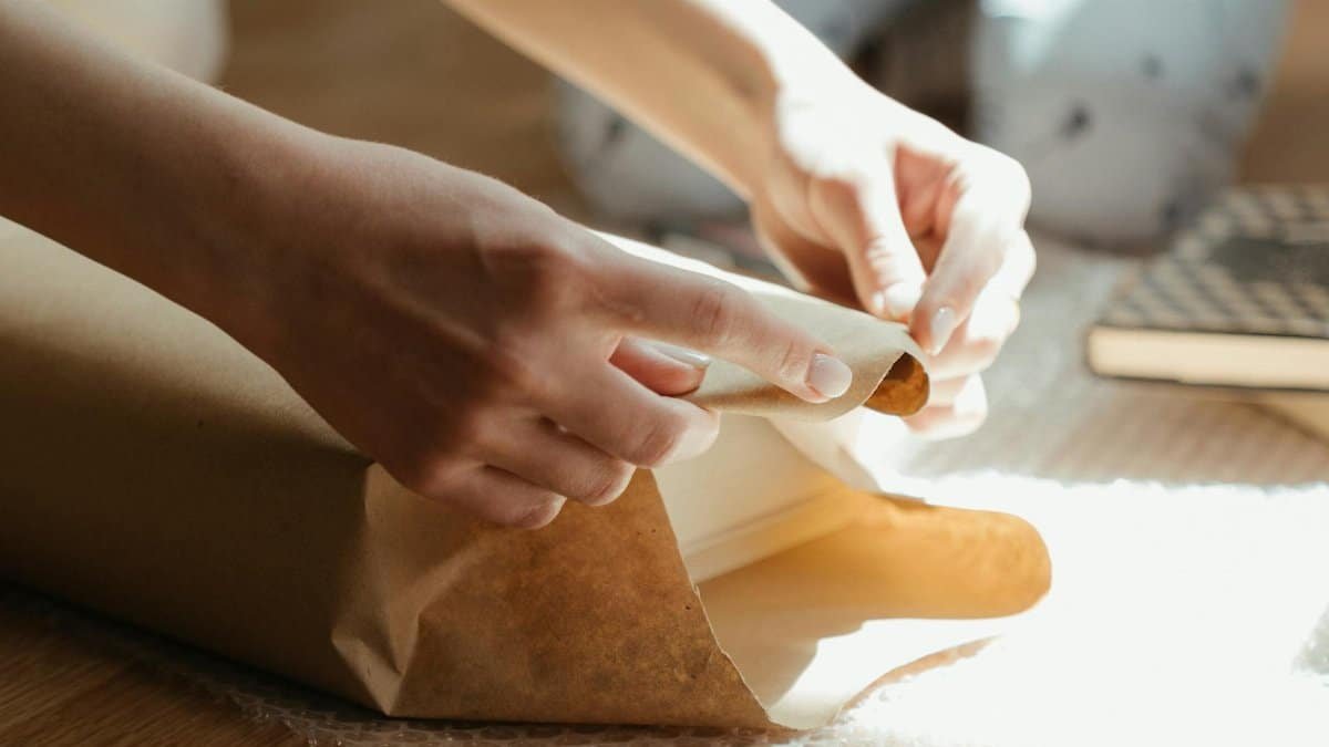 Hands wrapping an item in brown paper with sunlight streaming in, highlighting the texture and details.