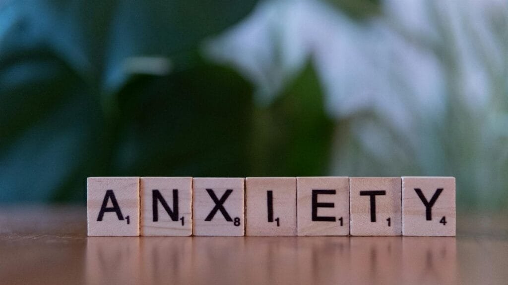 Close-up of wooden blocks spelling ANXIETY on a wooden surface with blurred green background.