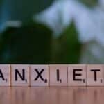 Close-up of wooden blocks spelling ANXIETY on a wooden surface with blurred green background.