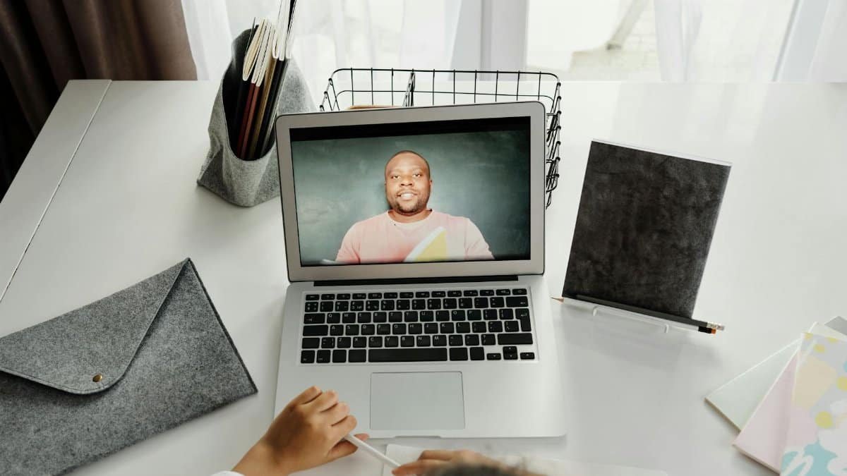 A student participates in a virtual class with a teacher on a laptop screen.