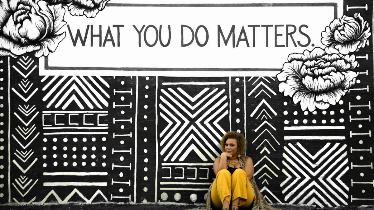 A woman sitting against a motivational mural reading 'What You Do Matters' in Birmingham, AL.