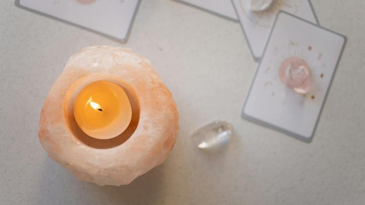 Himalayan salt candle holder with lit tealight surrounded by healing crystals and tarot cards for a spiritual ambiance.