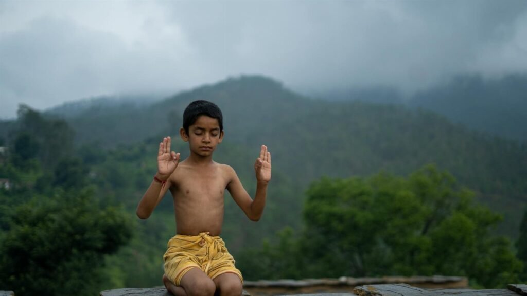 A young boy practices meditation outdoors with a peaceful mountain backdrop.