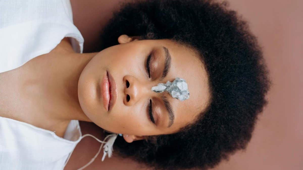 Woman practicing meditation with healing crystal on forehead, promoting wellness and relaxation.