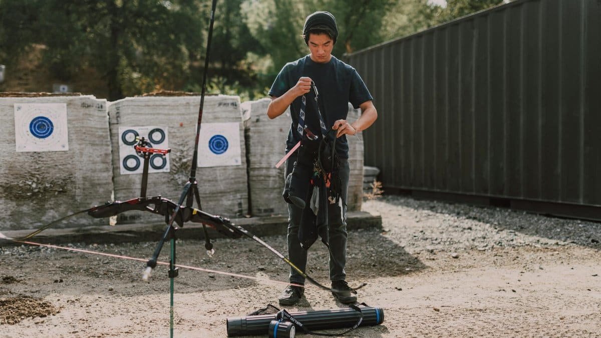 Teen adjusting equipment at an outdoor archery range, a focus on youth archery practice.