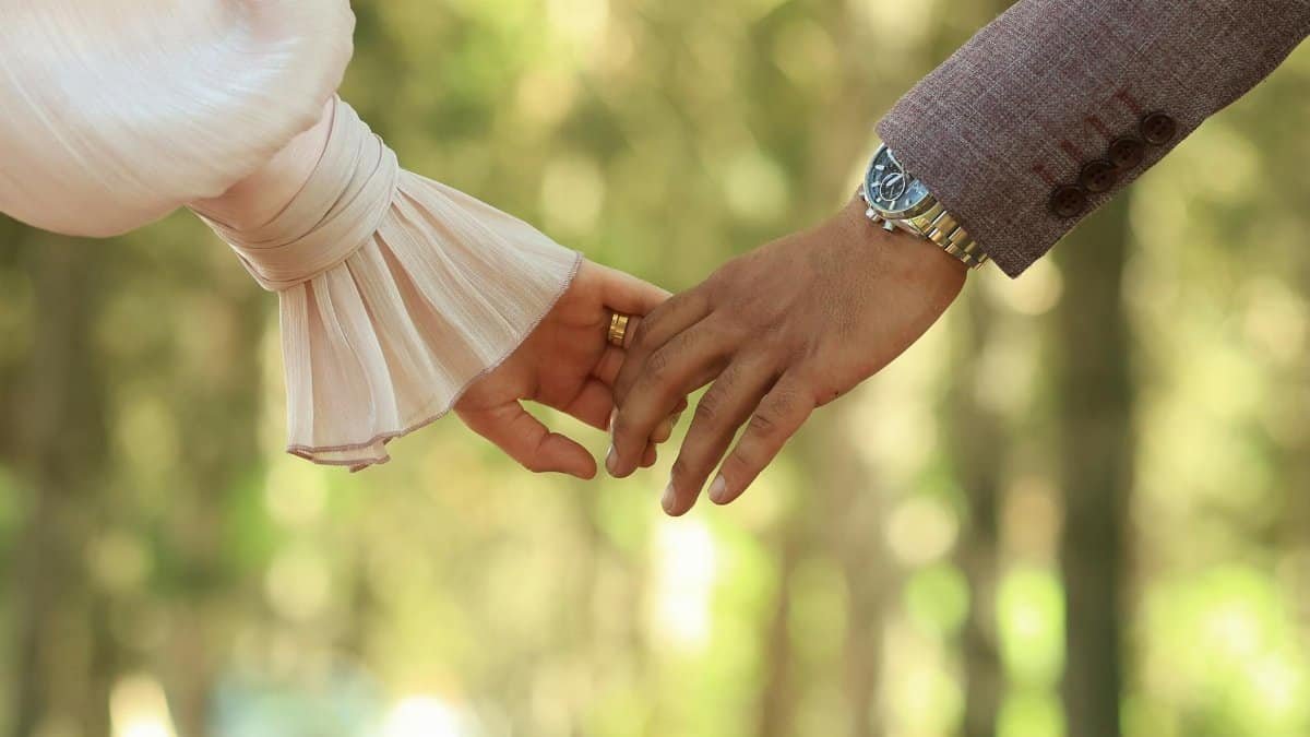 Romantic close-up of a couple holding hands in a sunlit forest setting.
