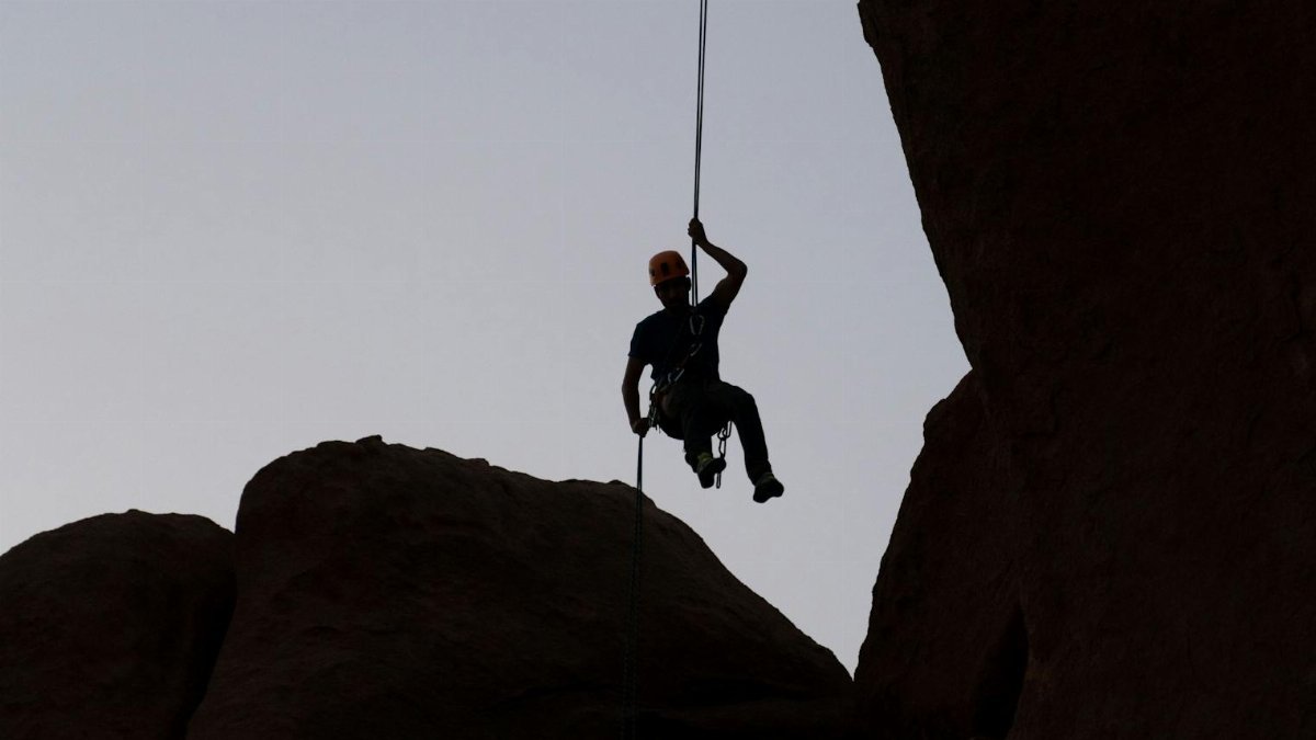 Silhouetted rock climber ascends at sunset, showcasing adventure and challenge.