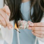 A woman burning sage for a cleansing ritual indoors, promoting tranquility and spiritual healing.