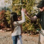 An instructor high-fiving a child at an archery range during a sunny day.