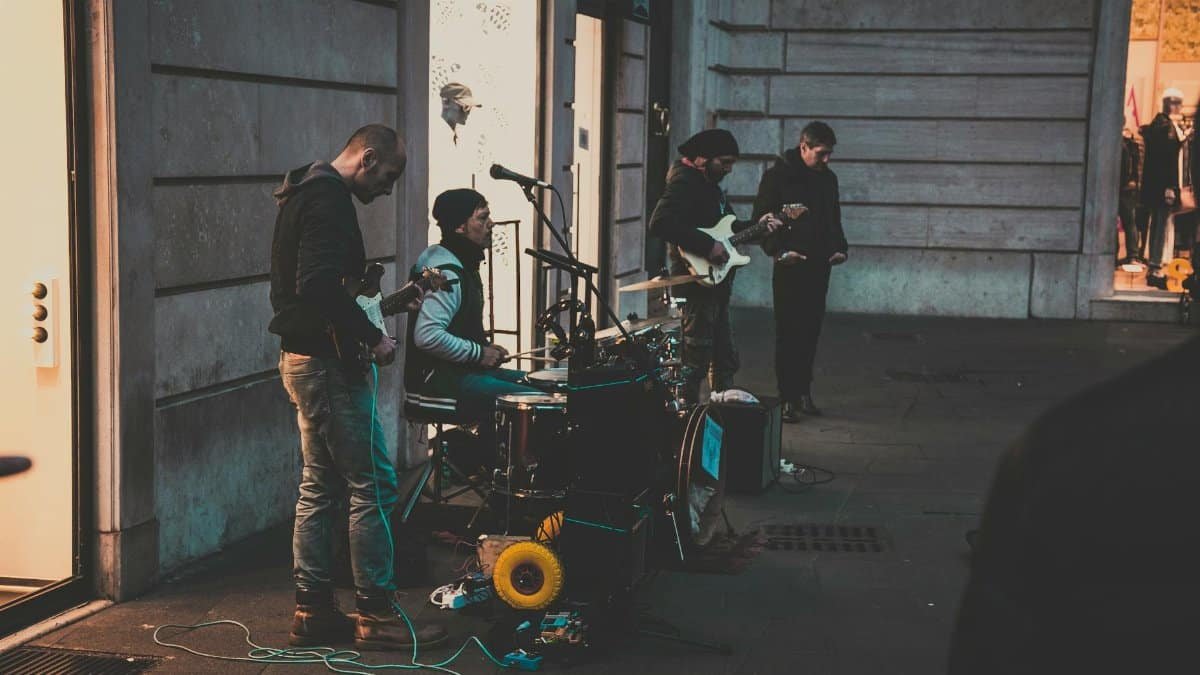 A group of street musicians performing with instruments on a city sidewalk during the evening.