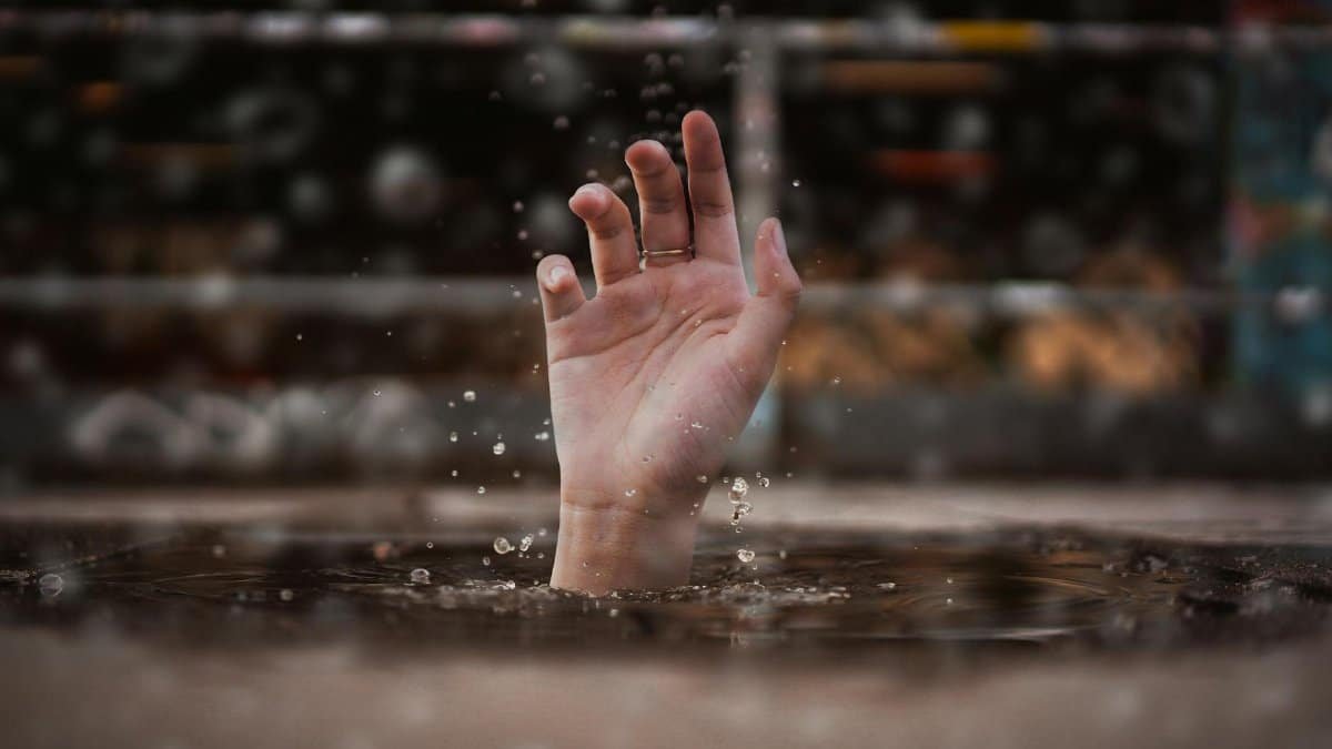 A single hand emerges from water, symbolizing a cry for help amidst a rainy setting.