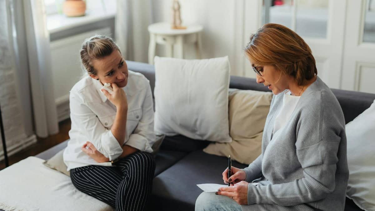 A thoughtful therapy session between two women in a cozy room.