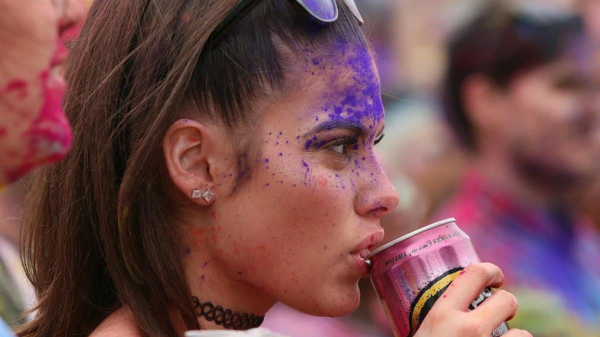 Young woman with colorful face paint enjoying a festival drink outdoors.