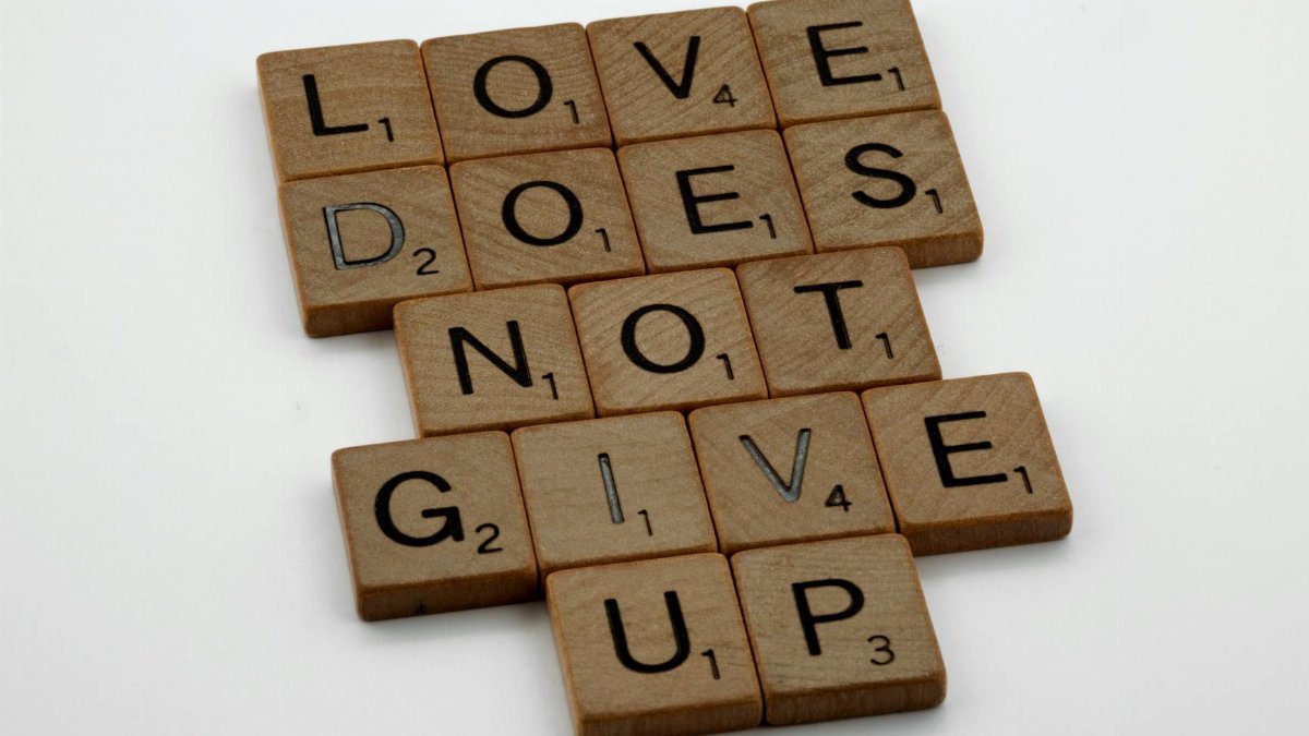 Wooden tiles on a white surface spell 'Love does not give up' in a motivational layout.