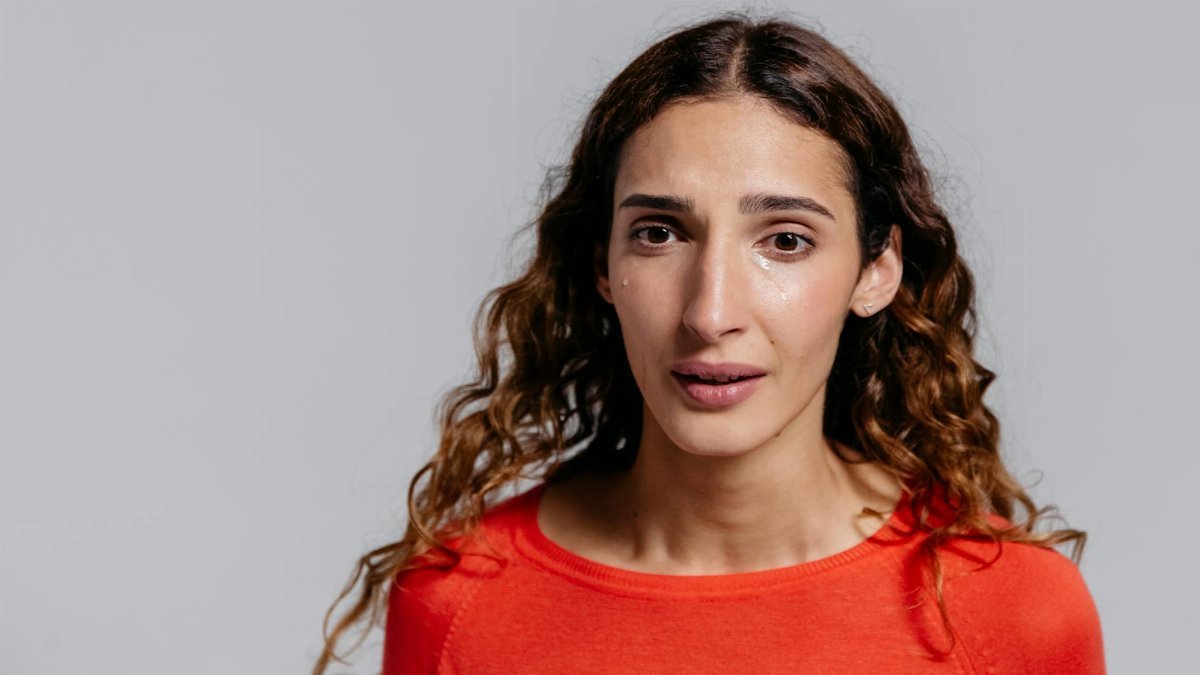 A woman in a studio displaying emotions and tears against a gray background.