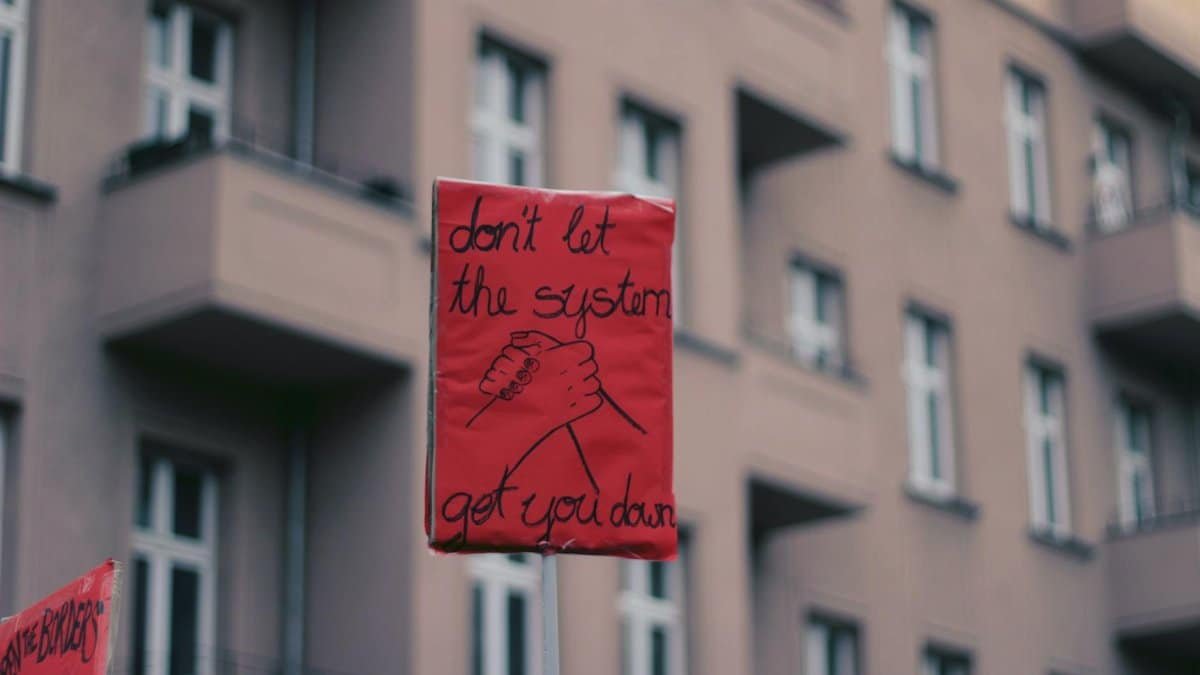 A red protest sign in Berlin reads 'Don't let the system get you down', capturing a rally's spirit.