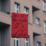 A red protest sign in Berlin reads 'Don't let the system get you down', capturing a rally's spirit.