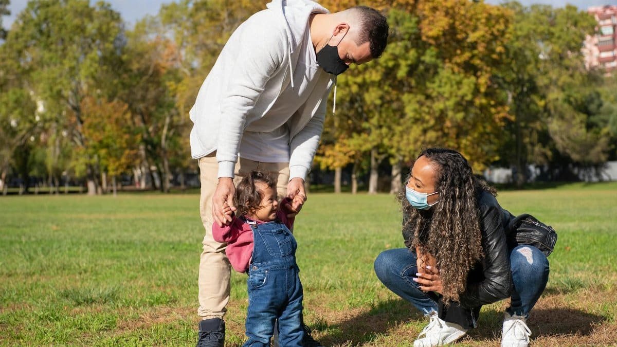 Parents with a small child wearing masks spending time in a park, embracing new normal.