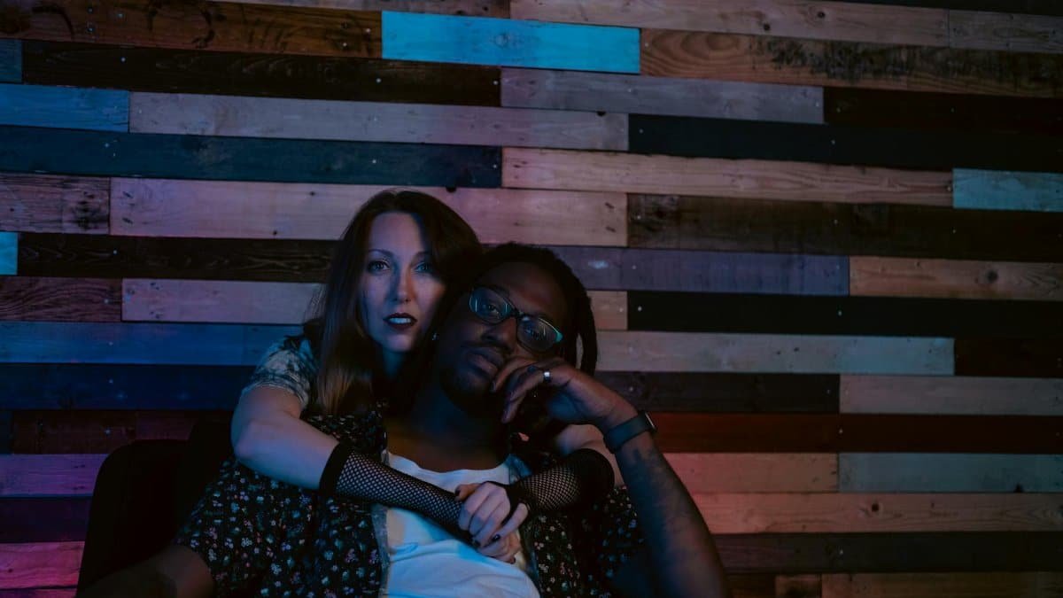 A fashionable couple embracing in a stylish lounge with a rustic wooden backdrop.