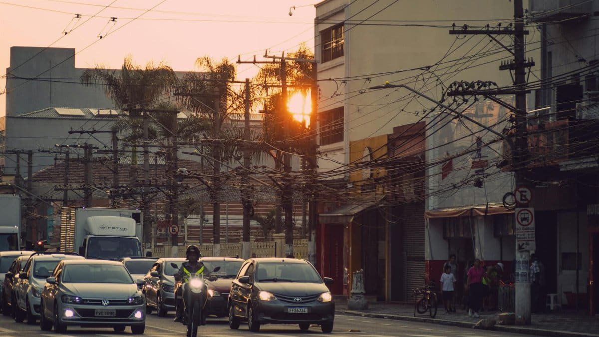 A bustling urban street with cars and motorbike at sunset. Cables and palm trees line the cityscape.
