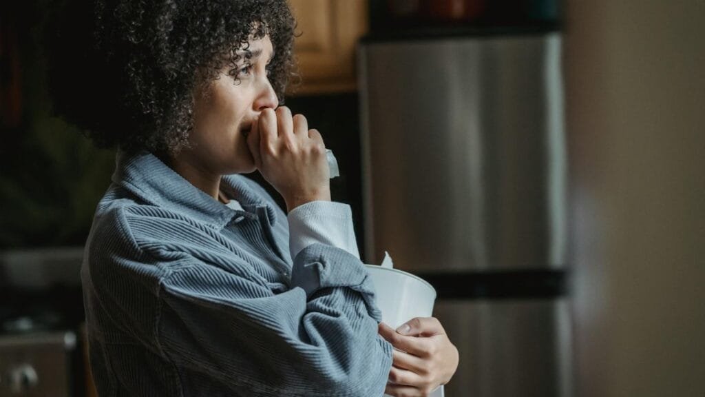 Side view of crying African American female with tissue sorrowing from unhappiness and grief in kitchen