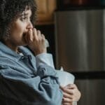 Side view of crying African American female with tissue sorrowing from unhappiness and grief in kitchen
