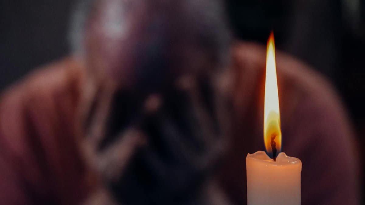 A senior adult in an emotional moment lit by a candle, symbolizing reflection and grief.