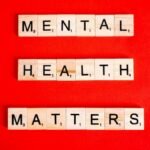 Wooden tiles spelling 'Mental Health Matters' on a vivid red background.