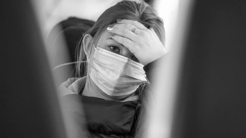 A woman wearing a face mask looks worried while traveling on public transport, emphasizing health concerns.