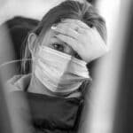 A woman wearing a face mask looks worried while traveling on public transport, emphasizing health concerns.