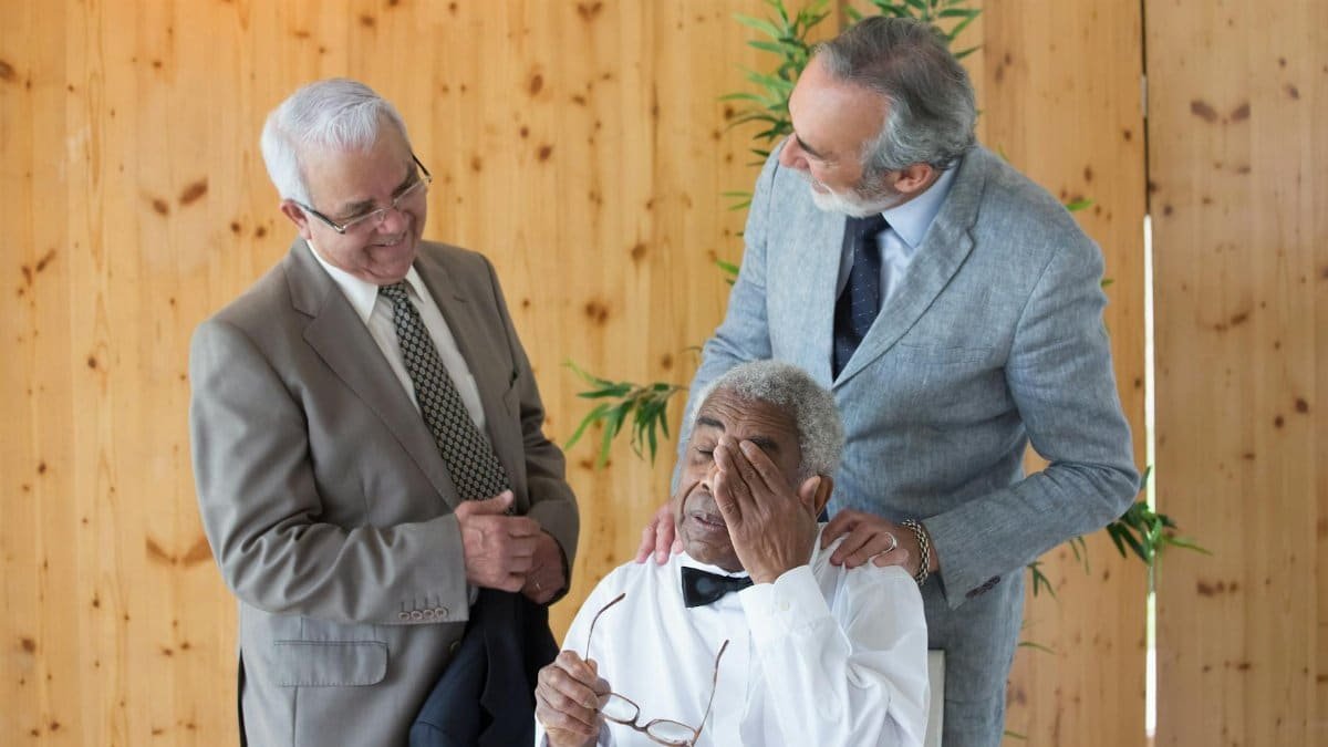 Three senior adult men sharing an emotional moment indoors, depicting friendship and support.