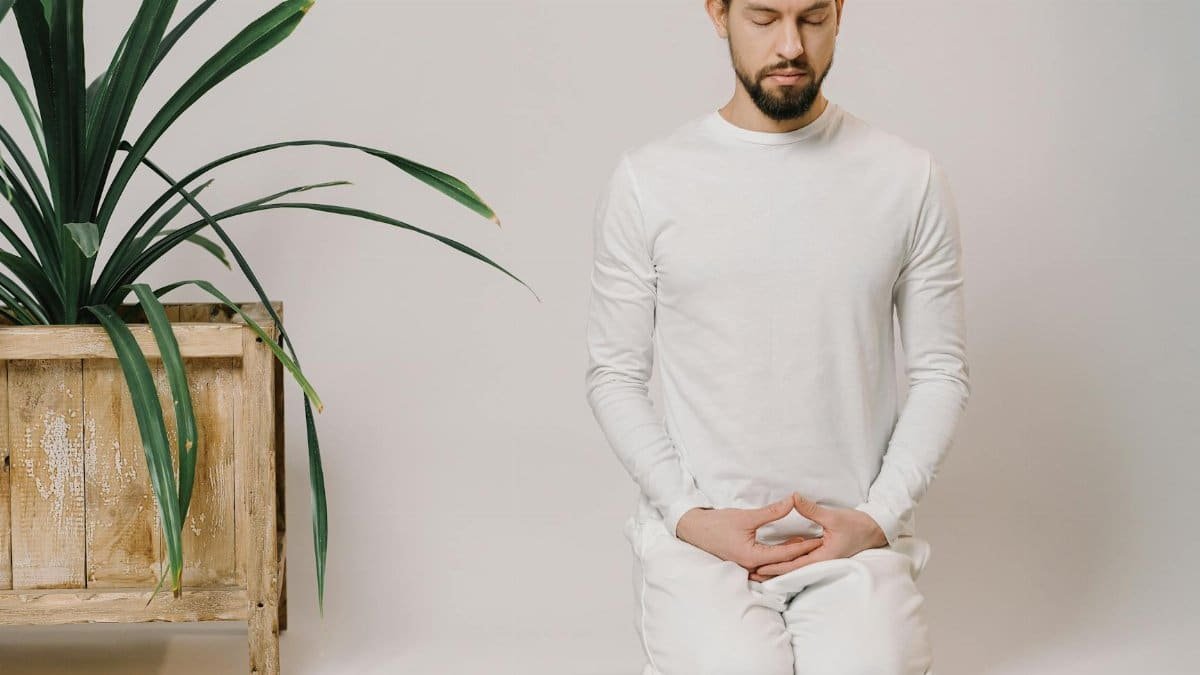 A man meditates indoors in a minimalist setting, focusing on relaxation and mindfulness.