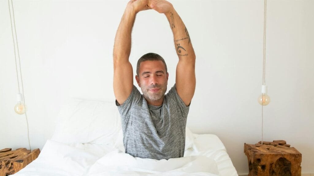 A man stretching his arms while waking up in bed, starting the morning with energy.