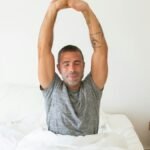 A man stretching his arms while waking up in bed, starting the morning with energy.