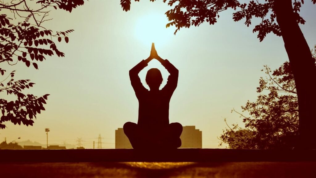 Silhouette of a person practicing yoga outdoors during sunrise, creating a calming atmosphere.