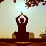 Silhouette of a person practicing yoga outdoors during sunrise, creating a calming atmosphere.