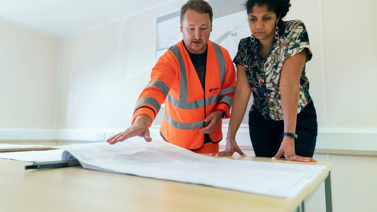 Two engineers reviewing blueprints in an office, discussing project details.
