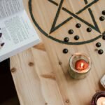 From above of crop unrecognizable fortune teller reading textbook at table with tarot cards and candles during divination process