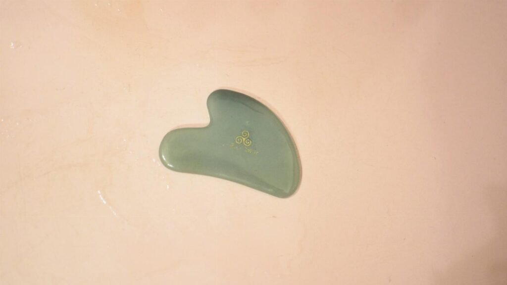 Top view of green shaped Gua Sha scraping massage tool placed in wet bathtub in bathroom during daily hygiene routine