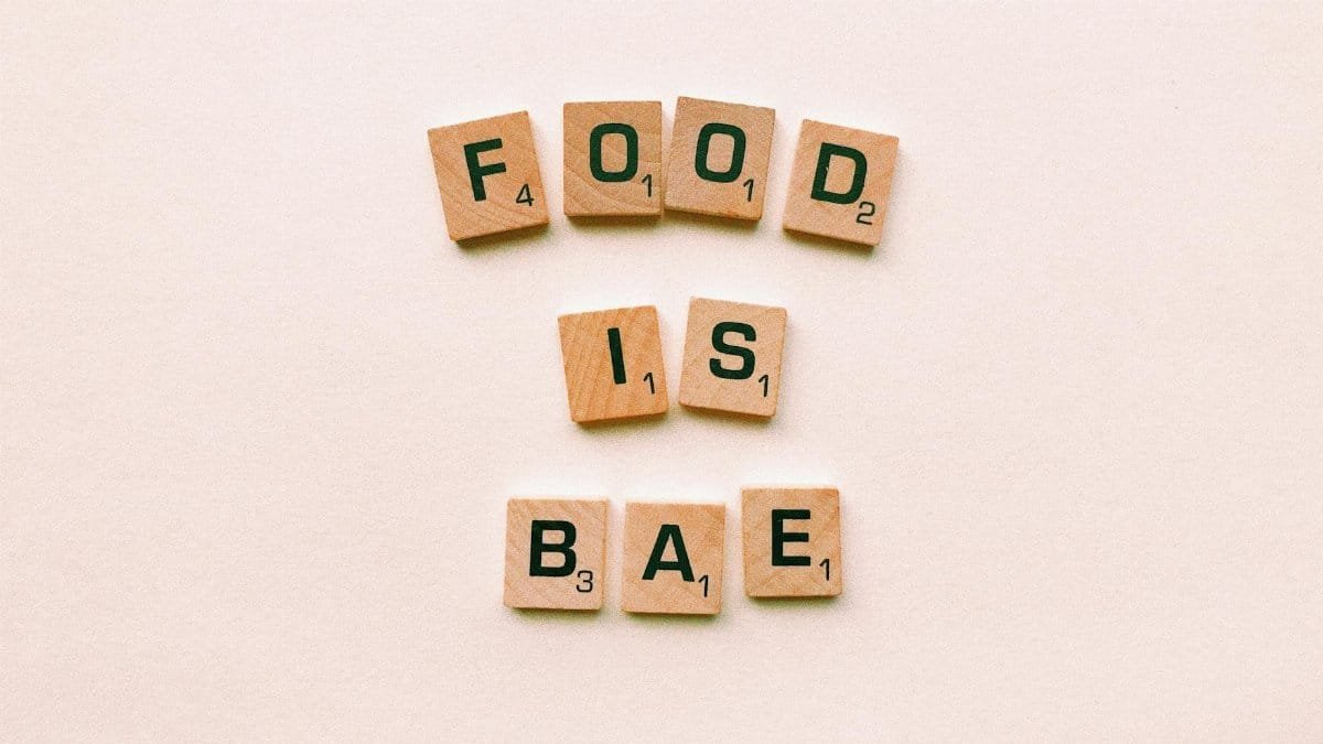 Scrabble tiles spelling 'Food is Bae' on a minimalist, textured background, emphasizing a playful message.