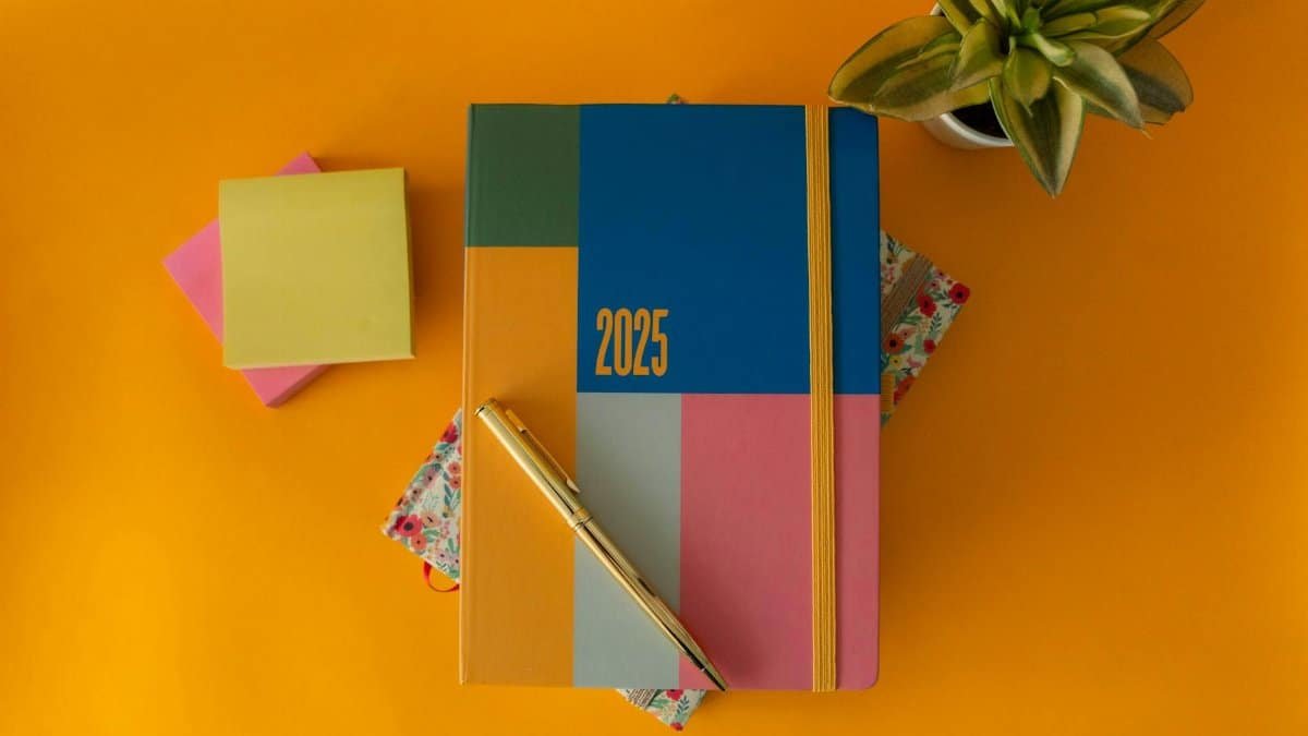 Flat lay of a vibrant 2025 planner with a pen and green plant on yellow background.