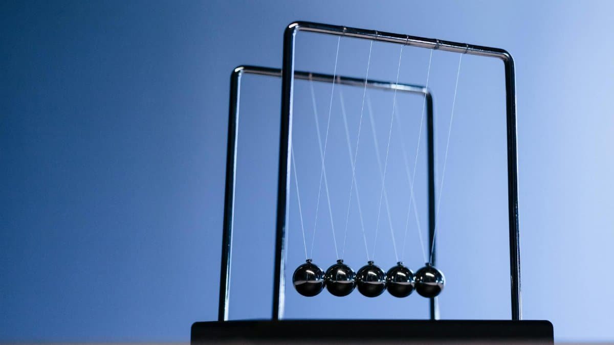 Silhouette of Newton's cradle with metallic balls against a blue background, showcasing physics in action.