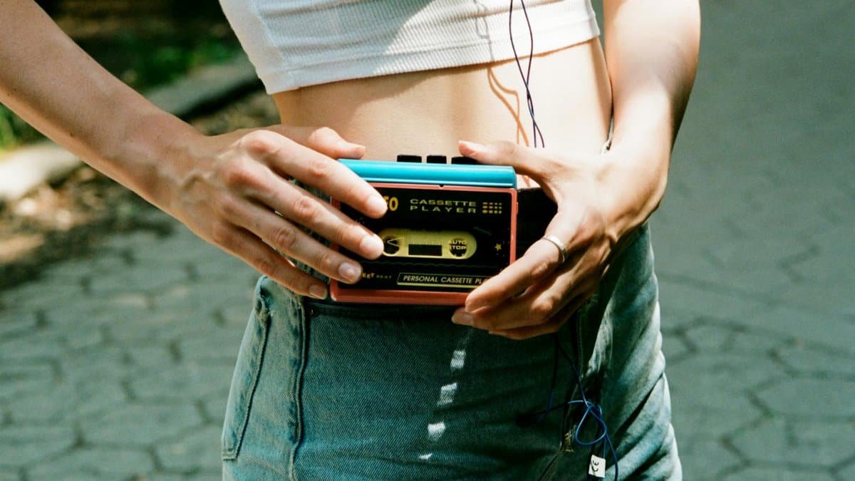 Woman holding a cassette player on a sunny day in New York City, capturing vintage vibes.