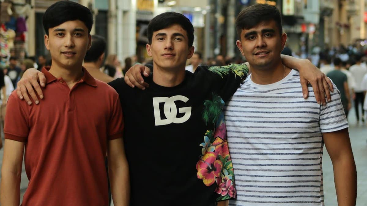 Three young men standing together, embracing in a bustling city street, capturing friendship and unity.